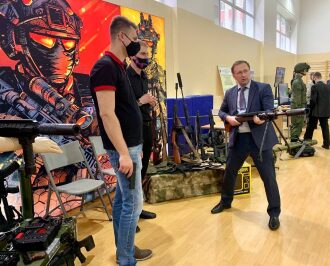Мужчина в костюме демонстрирует крупнокалиберную винтовку LASERWAR.